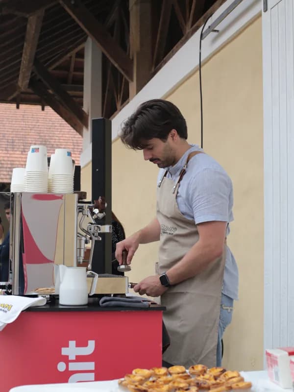 Gonçalo a compactar o café na máquina espresso, com a estrutura de madeira do telhado do pátio ao fundo.