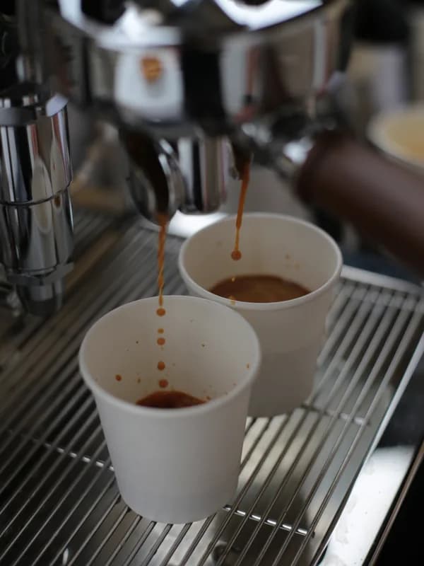 Extração de espresso a cair em dois copos de cartão, sob o bico duplo da máquina.