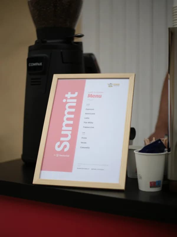 Placa do menu do Summit by Factorial com o logótipo Roam Coffee Bar, a listar as bebidas de café e chá disponíveis.