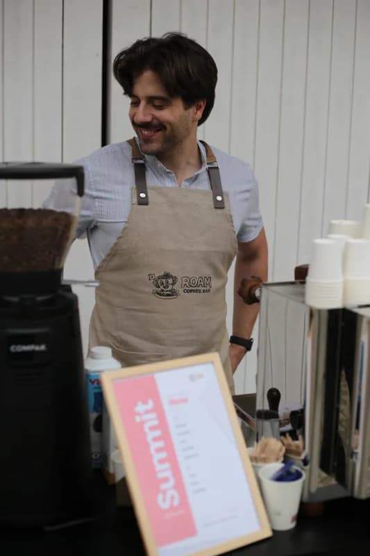 Gonçalo a sorrir atrás da barra, com o avental Roam Coffee Bar bem visível.